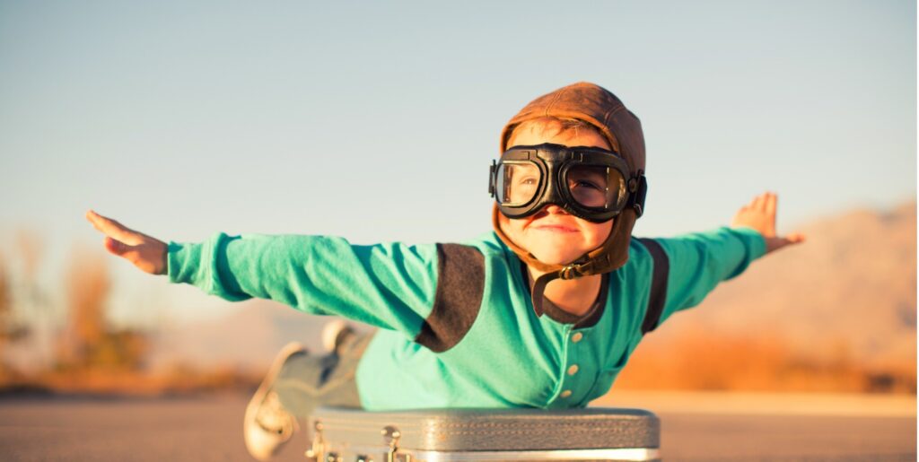 A young boy pretending like he's flying on a suitcase