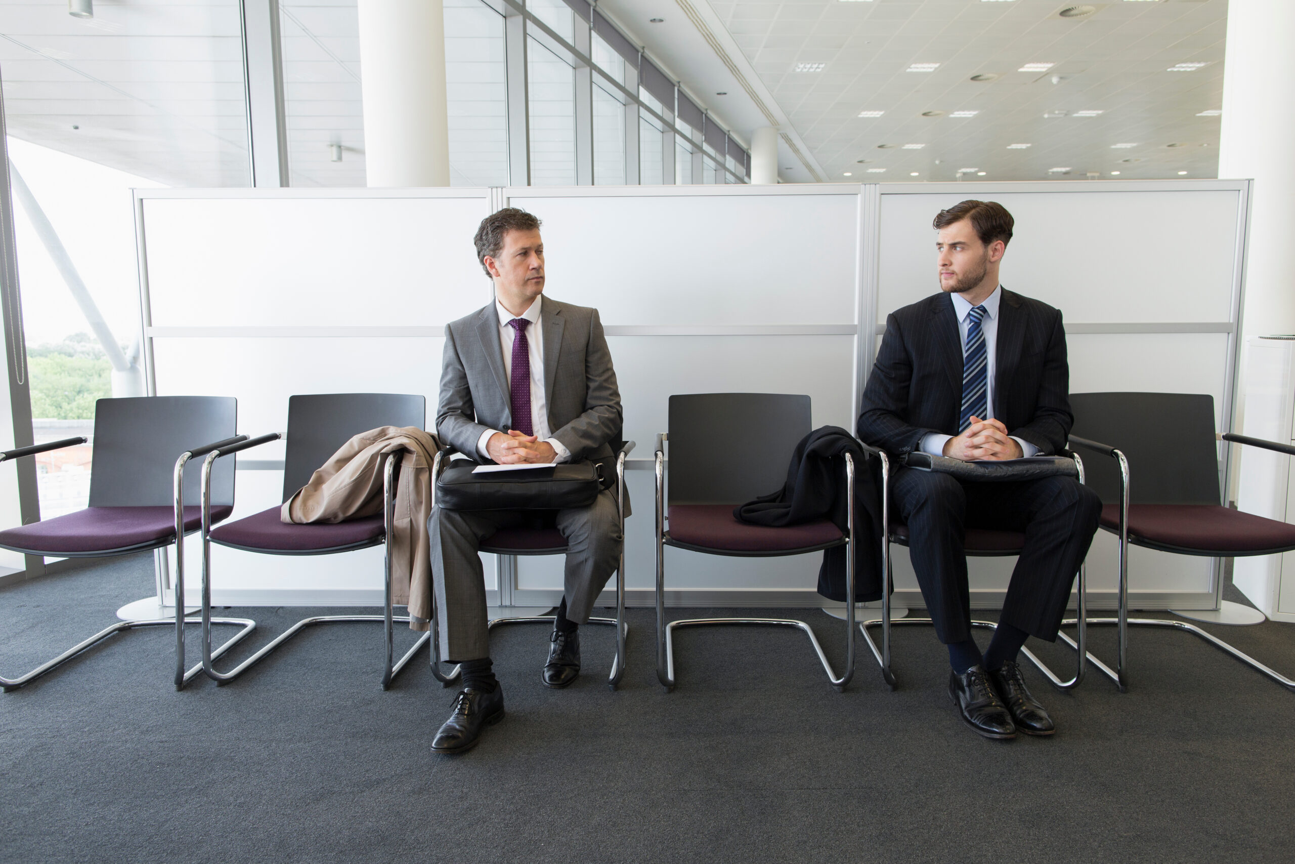 Competing businessmen waiting for job interview in office lobby