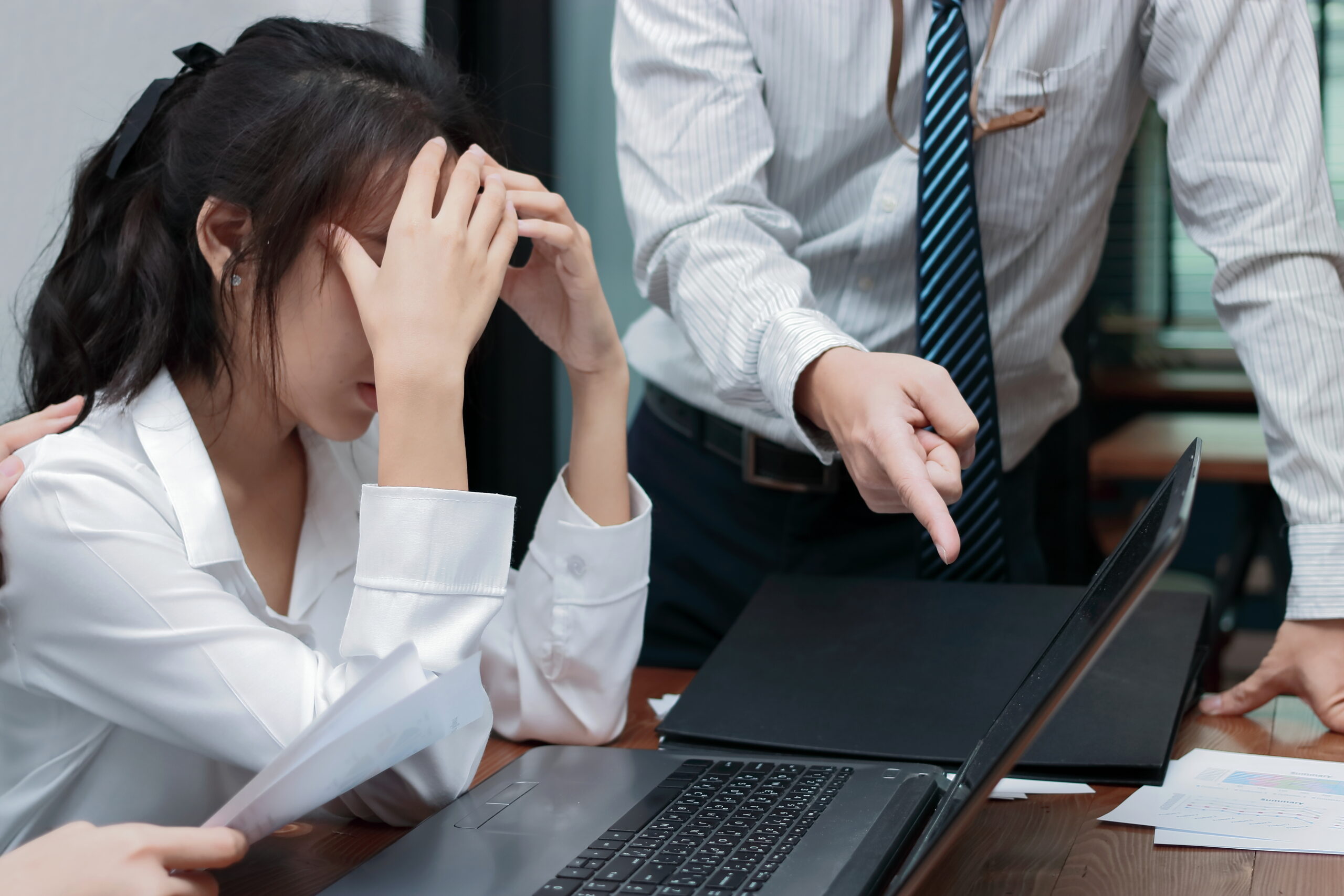 Angry boss blaming young Asian woman with hands on face in offic