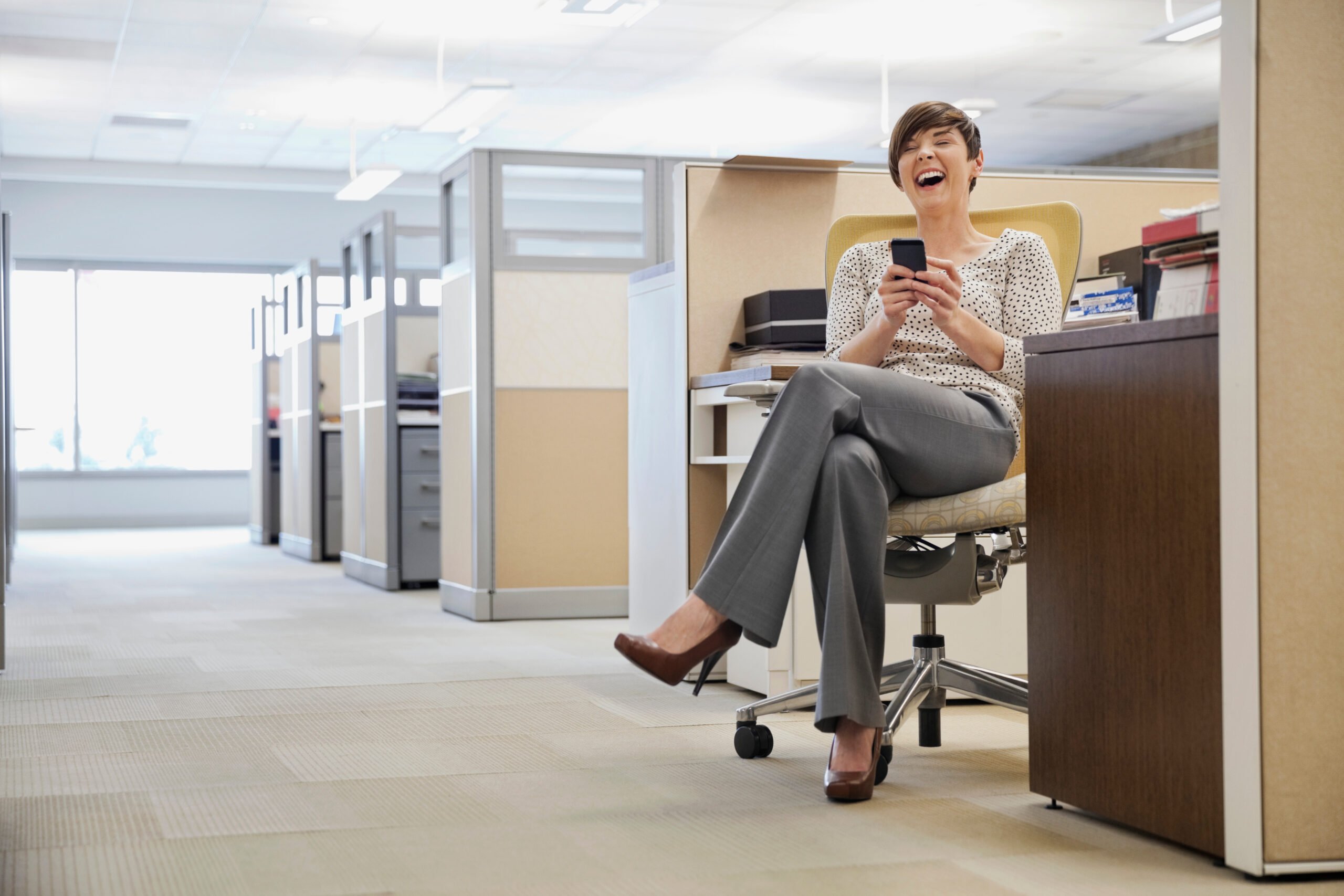 Laughing businesswoman text messaging on mobile phone in office