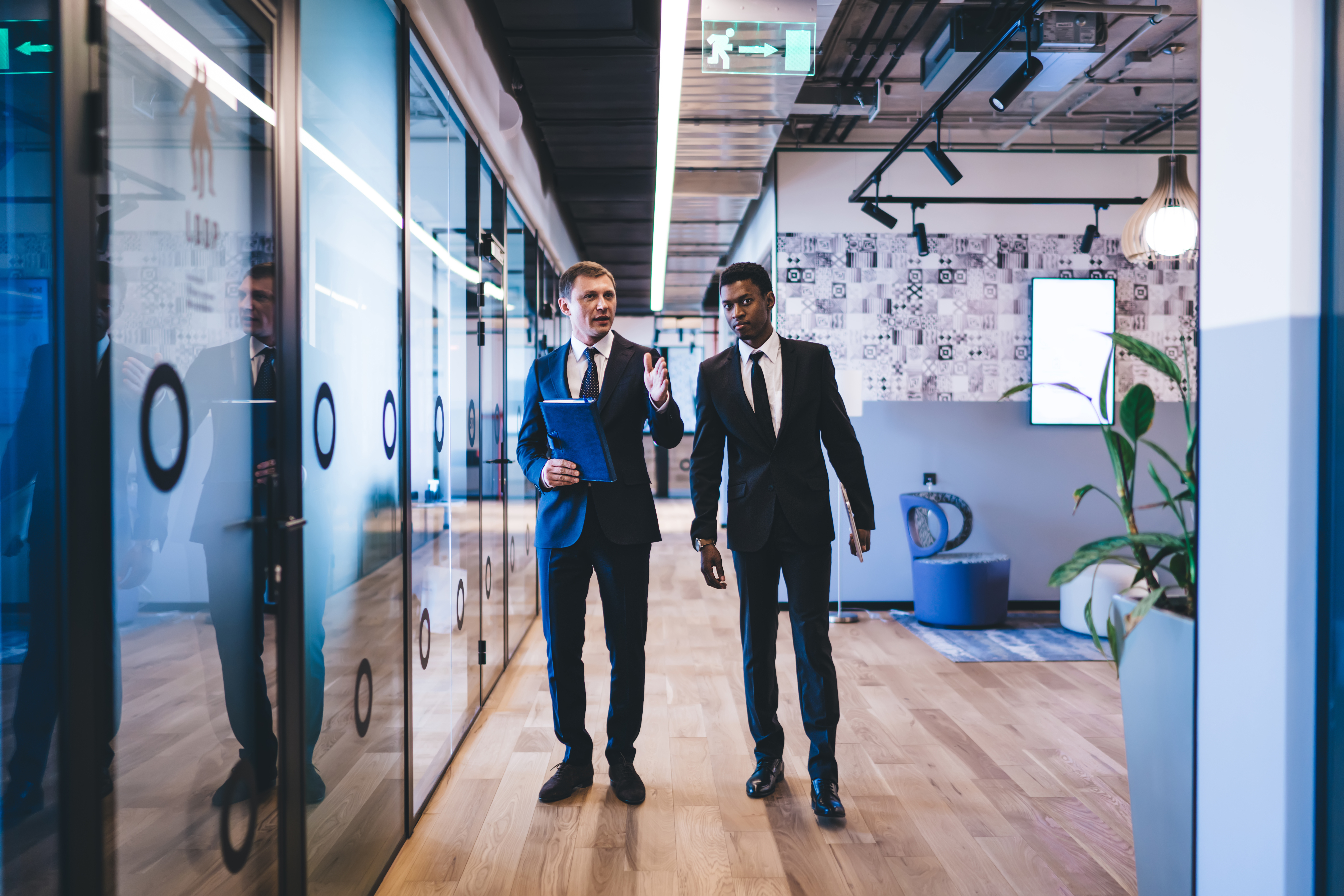 Male managing director in formal suit giving tour around stylish office centre new African American hire while telling about official powers