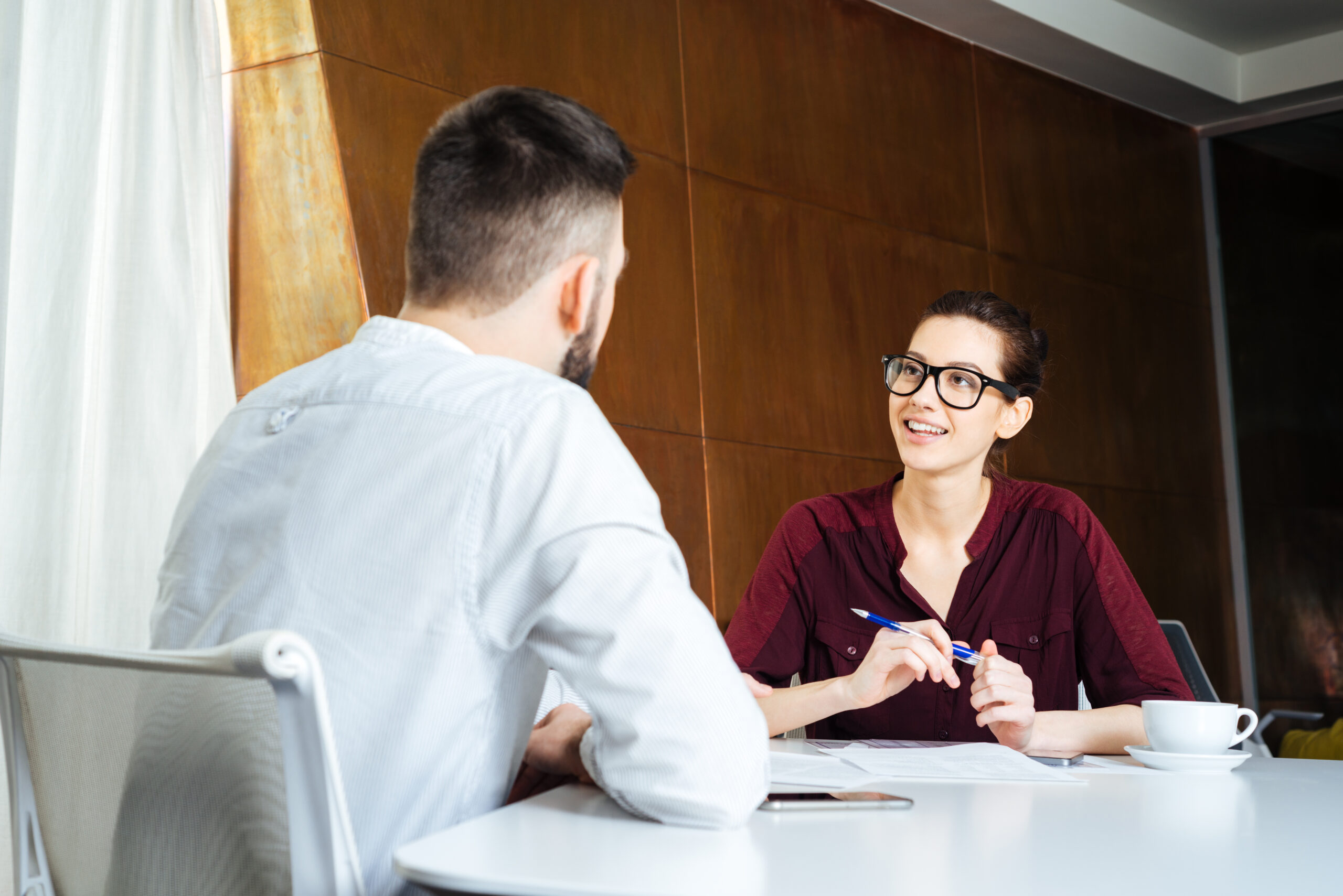 Smiling beautiful businesswoman in glasses talking to young businessman in meeting room