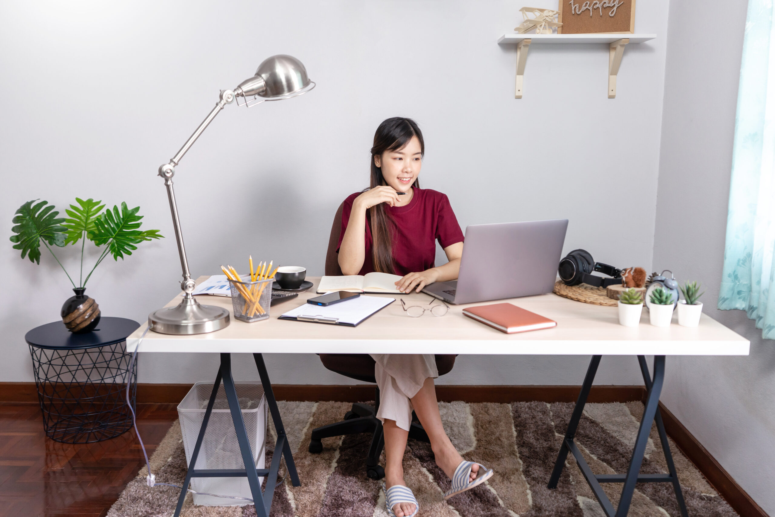 A young, beautiful relaxing business asian girl use a laptop working remotely from home on desk as a freelancer, quarantine for Coronavirus and smart working concept. A young woman working in a home office