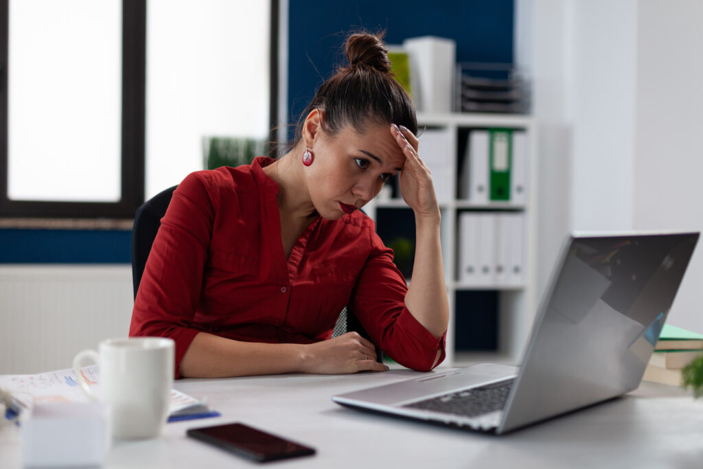 Tired businesswoman sitting at startup business desk looking at laptop screen.