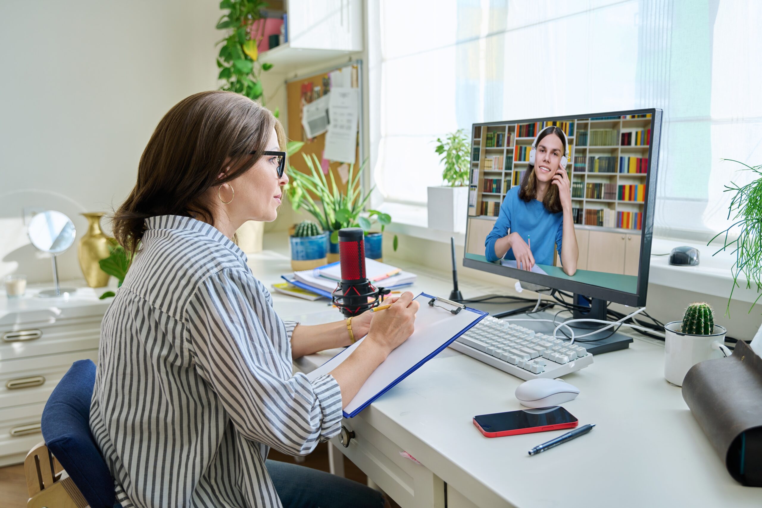 Mature woman talking online with teenage male using video call on computer, home interior. Virtual meeting, therapy session with psychologist. Chat conference technology psychology education learning