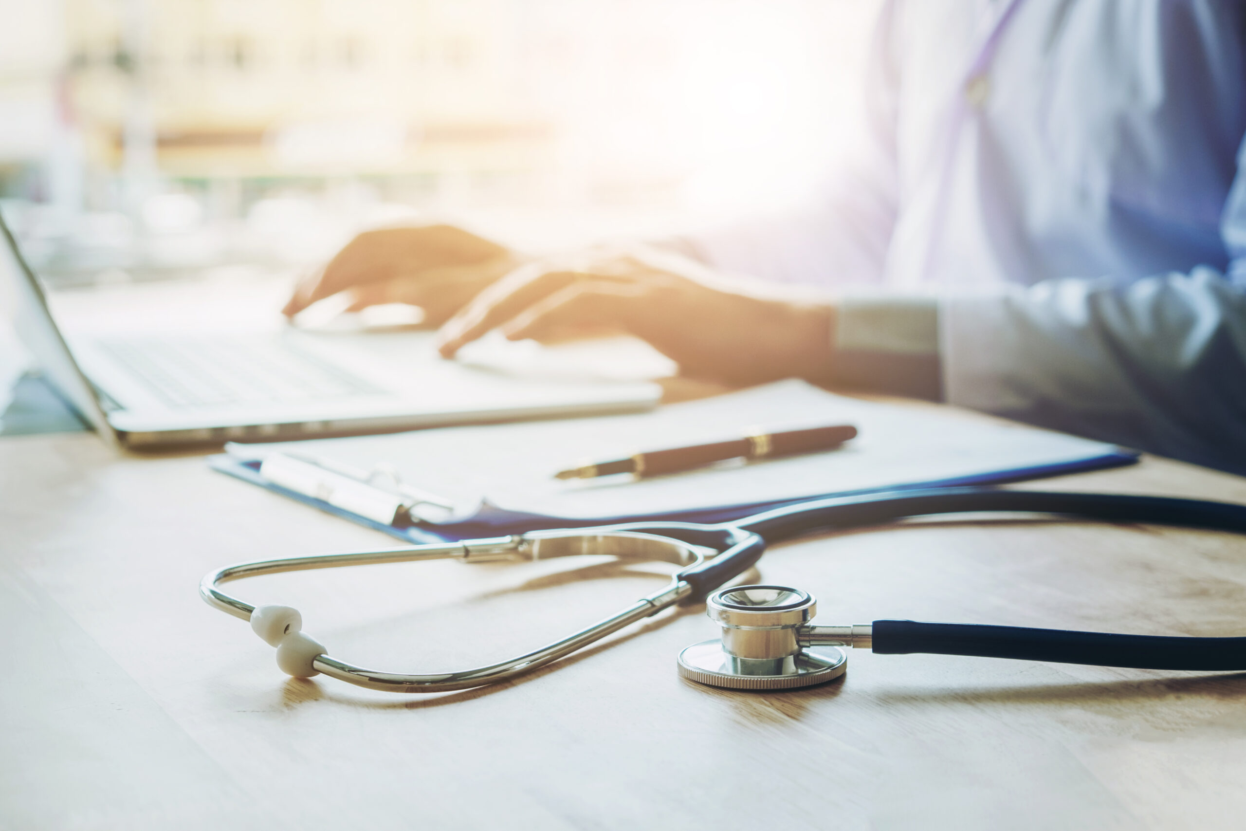 Doctor typing information on Laptop in Hospital office focus on Doctor typing information on Laptop in Hospital office focus on Stethoscope