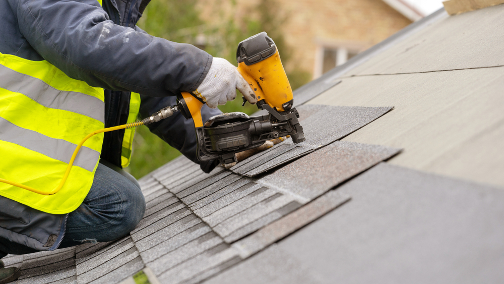 A construction worker using a nail gun to put shingles on a roof